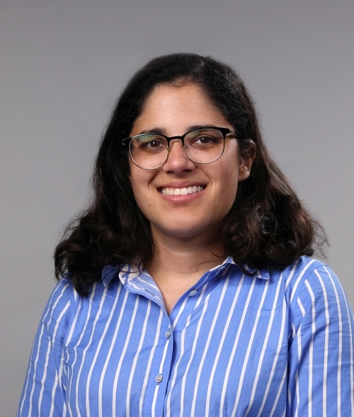 a woman with dark hair wearing glasses and blue striped collared shirt on a grey background