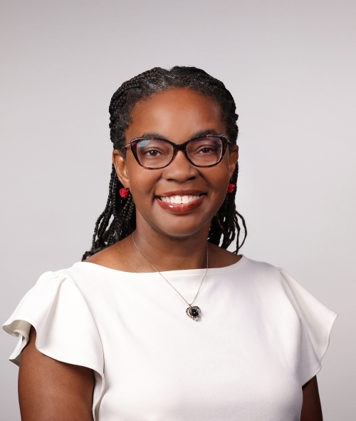 a Black woman with dark hair wearing a white top and glasses on a grey background