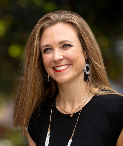 a woman with dirty blonde hair wearing a black top and silver jewelry