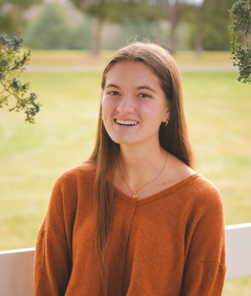 a young woman with brown hair wearing an orange sweater
