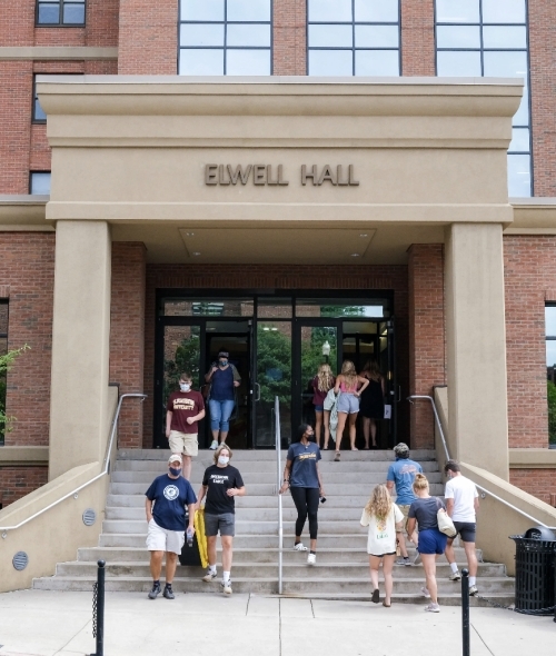 Stock image of students walking down the stairs on a college campus wearing masks