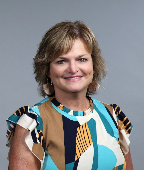 Woman with blonde layered hair and colorful blue and tan blouse