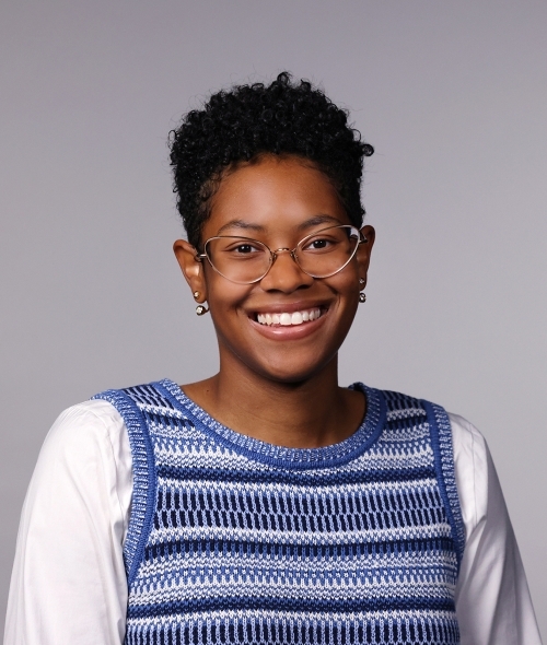 Woman with a blue striped vest, white shirt, glasses, and short hair