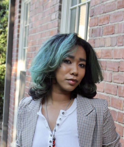 a professional wearing a grey blazer with dark hair smiling in front of a brick building