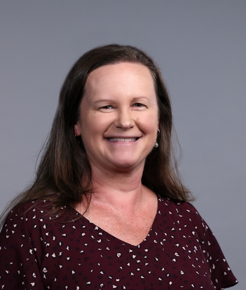 a woman with long dark hair wearing a red polka dot top on a grey background
