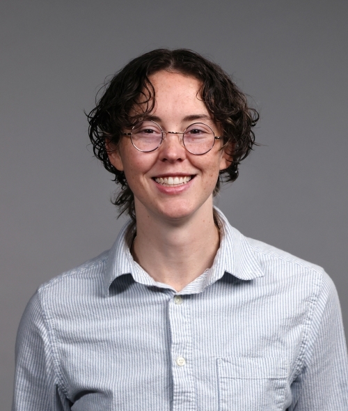 a young person wearing a collared shirt with short curly hair and glasses on a grey background