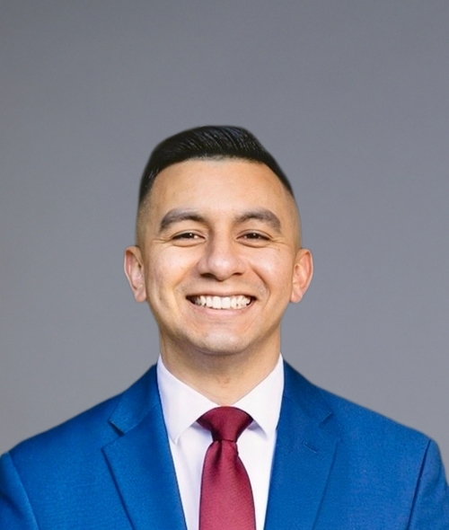 a young man with short dark hair wearing a suit and tie on a grey background