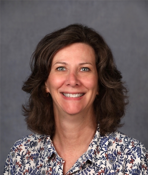Woman with curly brown hair and floral blouse smiles at the camera