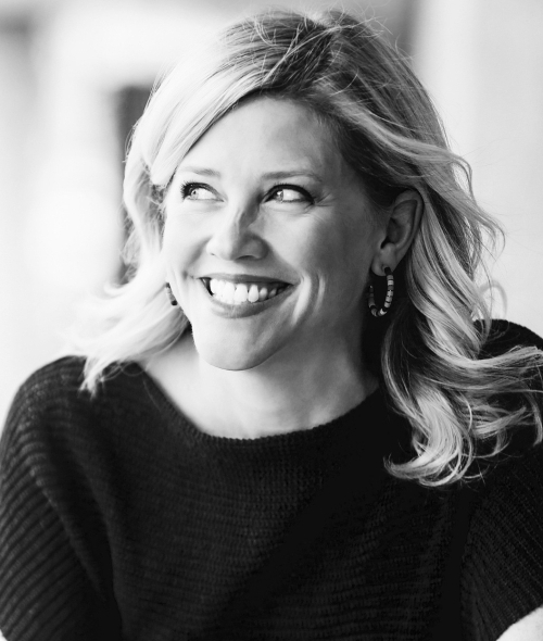 Greyscale image of a smiling white woman, looking to her right, with shoulder length blonde hair