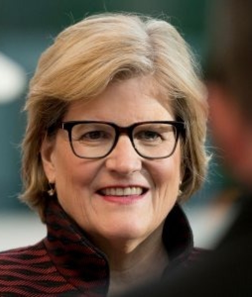 Clayton Spencer smiles while wearing black-rimmed glasses and a dark red and black patterned top.