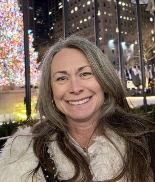 a woman with dark hair smiling outside at night while wearing a coat