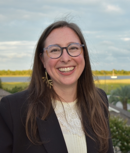 a young woman with long brown hair wearing glasses, a white blouse and a black blazer