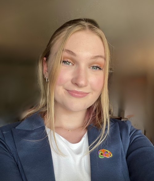 Blonde woman, likely in her 20s, takes a selfie in a blue blazer and white blouse
