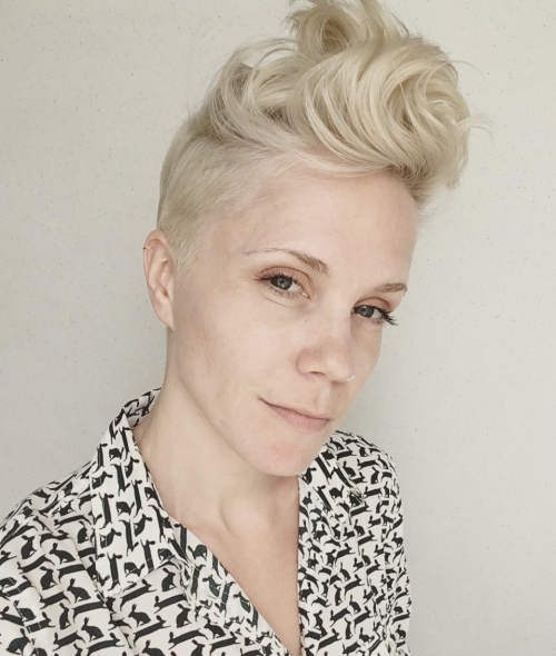 A person with platinum blonde hair in a pixie cut and a black and white blouse