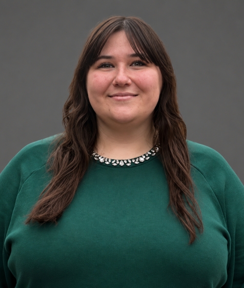 A woman with long brown curled hair, a green blouse and a sparkly necklace