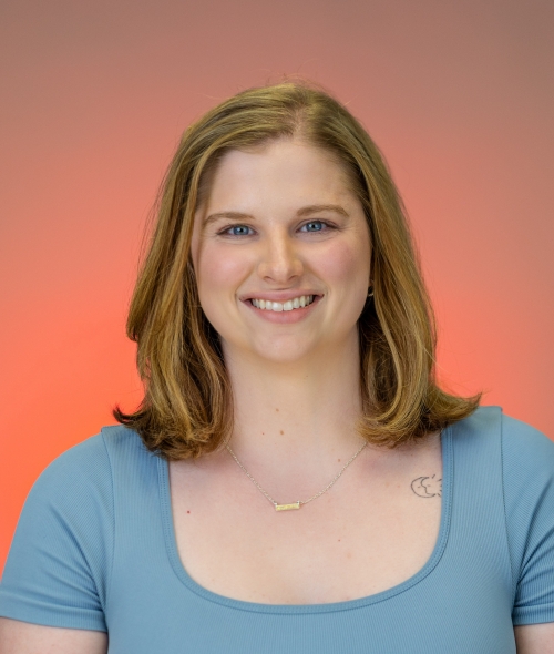 Savannah smiles warmly with shoulder-length blonde hair and blue eyes, wearing a blue scoop-neck top against a warm orange-and-gray gradient background.