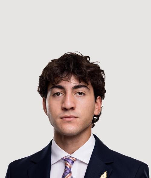 A male student in a suit and pink striped tie with dark curly hair and a neutral expression