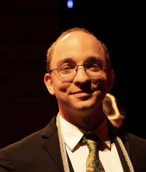 A man with short dark hair, round glasses, and a suit and tie