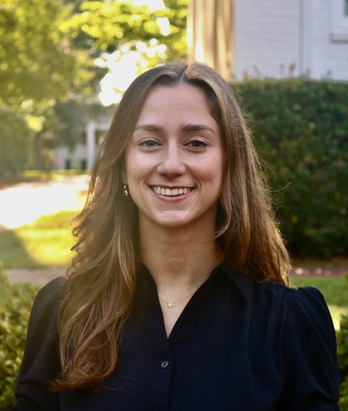 Ann smiling outdoors wearing a black button-up shirt with long brown hair