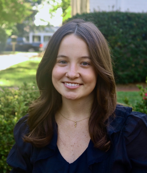 Annalee smiling outdoors with shoulder-length wavy dark hair and a black top.
