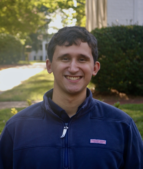 Greg smiling outdoors in a dark blue quarter-zip pullover