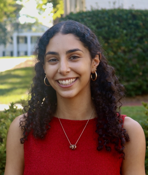 Maya smiling outdoors with curly dark hair and a bright red top