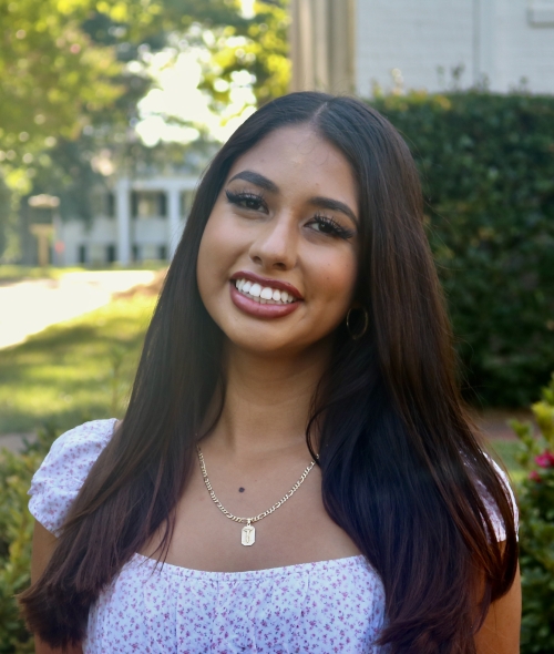 Priscila smiling outdoors with long dark hair wearing a floral print top