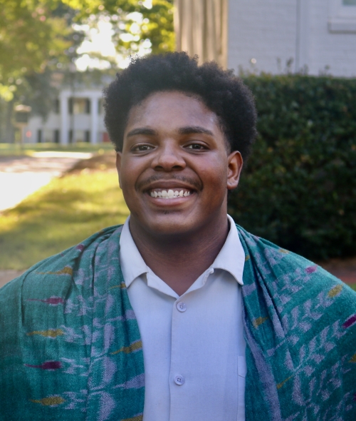 Romeo smiling outdoors in a light dress shirt draped with a patterned teal scarf