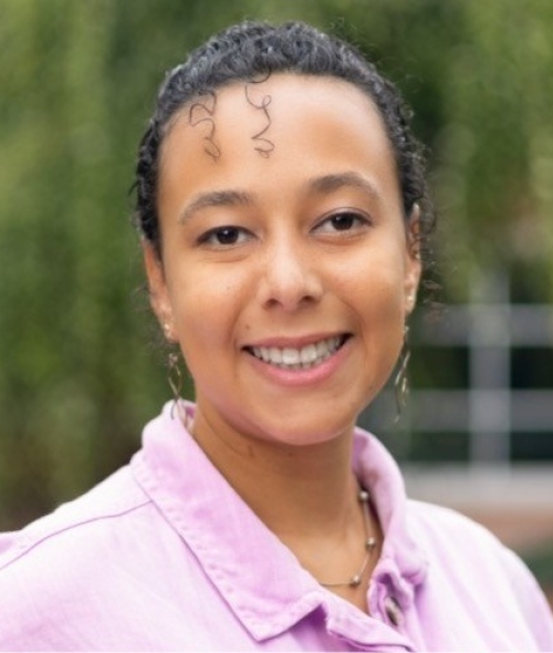 A woman with a pink collared shirt and curly, pulled back hair