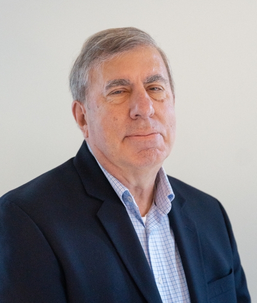 An older white man wearing a blue collared shirt and blazer with grey hair