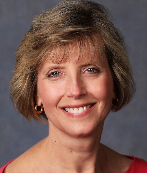 A woman with a red shirt, short blonde hair and bangs with a smiling expression