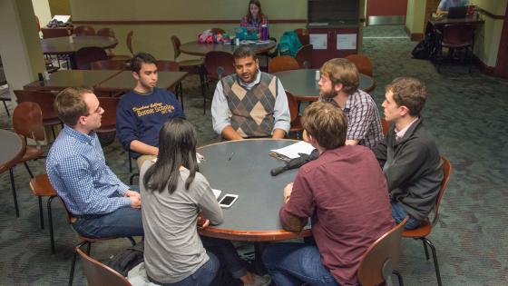 Professor and six students sit around a round table in the Union discussing economics