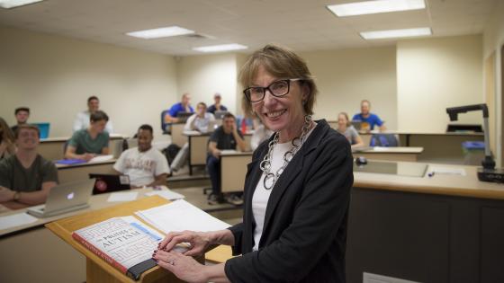 Prof. Roberts smiles at camera while leading class from podium