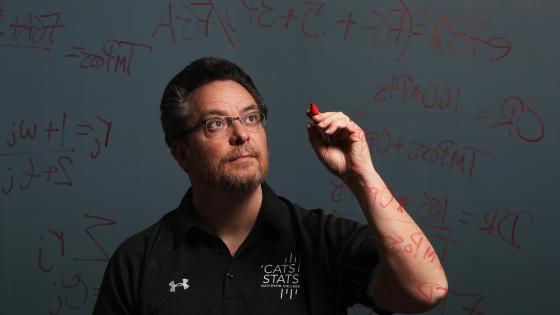 Tim Chartier writes math equations on a glass board