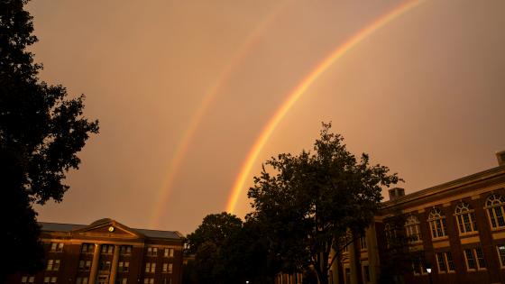 Sky rainbow over college buildings and trees 