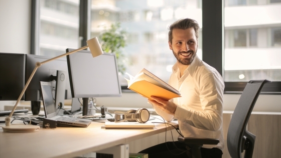 Man at computer holding a book while at work