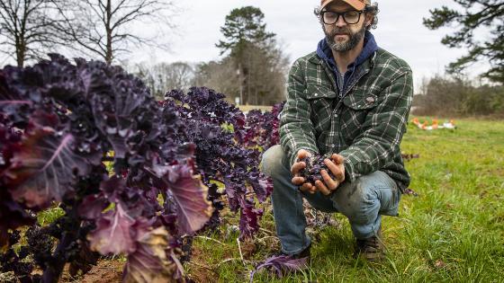 Joe Rowland kneels with Produce at Davidson College Farm