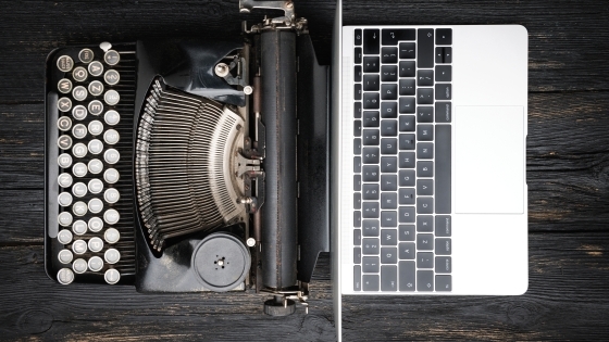 Antique typewriter next to modern laptop on wooden table