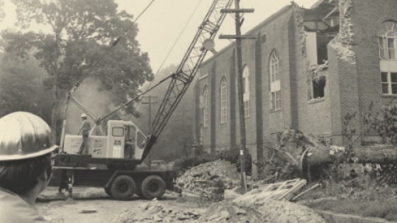 black and white photo of construction machine tearing down walls of former Johnston Gymnasium