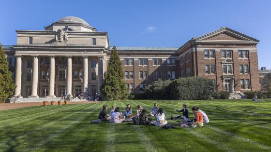 students sitting in circle outside on grass field outside Chambers building