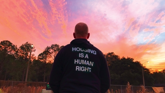 Photo of man facing away wearing sweatshirt that reads "Housing is a Human Right"