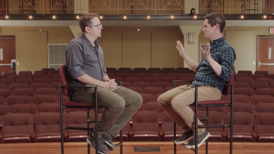 Two men facing each other in chairs onstage