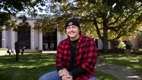 Jake Fernicola, a male student in a black beanie hat and red flannel sitting outside