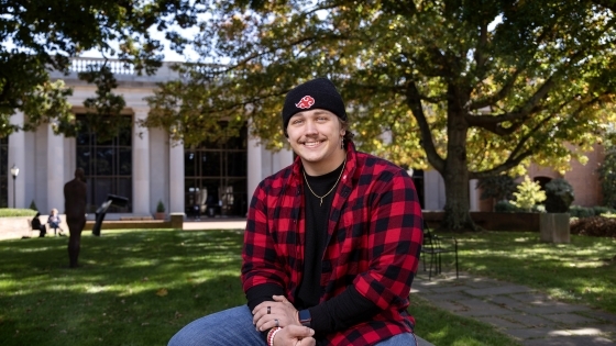 Jake Fernicola, a male student in a black beanie hat and red flannel sitting outside