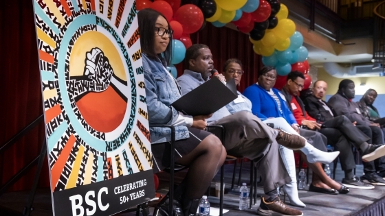 panel of people on stage with a sign in foreground that says "BSC Celebrating 50+ Years"