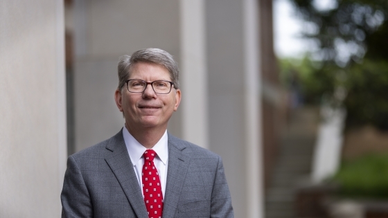 A white male wearing a grey suit and a red tie