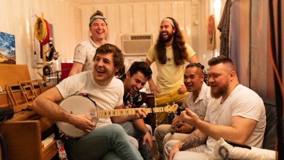 A group of young men sitting together and smiling while one holds a banjo