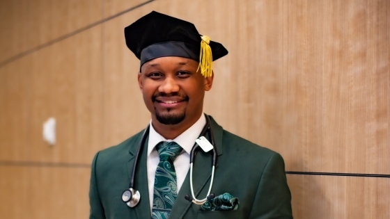 a young man wears a graduation cap and suit and holds a sign that says "I matched Pediatrics at Childrens Hospital of Philadelphia"