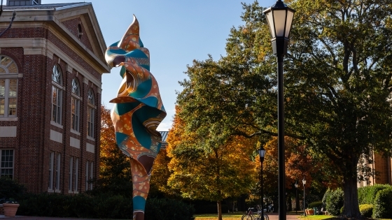 a brick building surrounded by trees with fall foliage and a colorful sculpture