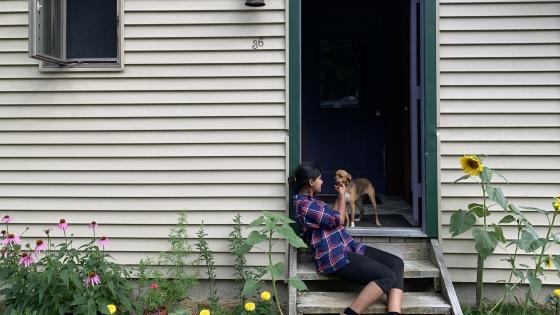 a young woman sits on a staircase outside of a house with a dog surrounded by flowers